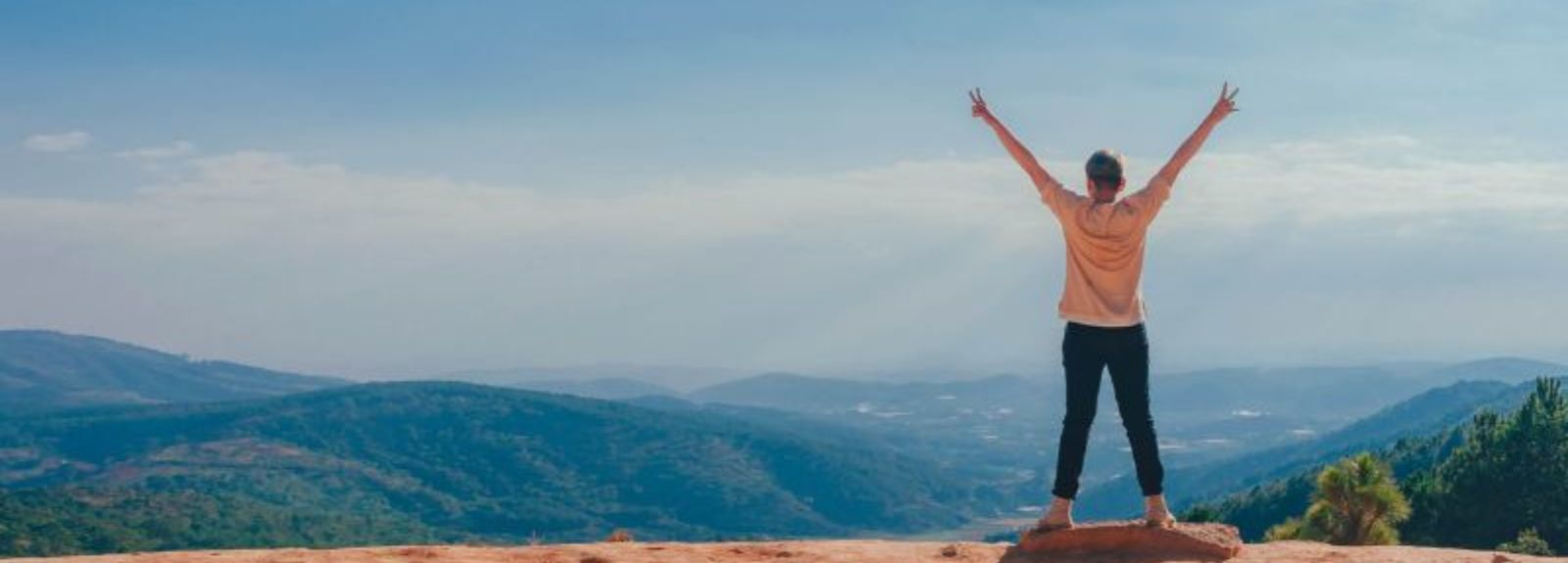 student standing on a cliff top with arms stretched out